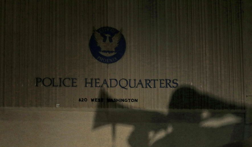 FILE - This July 8, 2016 file photo shows the shadow of a protester with a bullhorn in front of Phoenix Police Department headquarters as hundreds of marchers take to the streets to protest against fatal shootings of black men by police, in Phoenix. Phoenix City Council members Tuesday, Feb. 25, 2020, voted 5-4 to approve a citizen review board with the power to investigate police after a raucous meeting that stretched five hours into the evening. The council has been examining different proposals for policing the police after a record number of officer shootings in past years and the uproar over a videotaped encounter last summer between officers and a black family whose young daughter took a doll from a dollar store. (AP Photo/Ross D. Franklin, File)