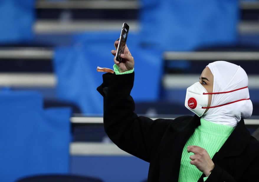 A fan wearing a protective mask takes a picture with her cell phone prior the Champions League, round of 16, first leg soccer match between Real Madrid and Manchester City at the Santiago Bernabeu stadium in Madrid, Spain, Wednesday, Feb. 26, 2020. (AP Photo/Manu Fernandez)
