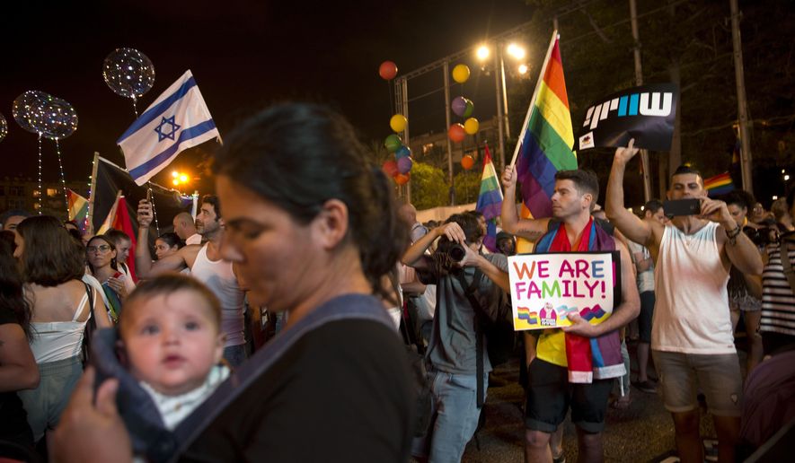 FILE - In this July 22, 2018 file photo, Israelis wave flags and hold signs during a rally to protest against inequality for the LGBT community in Tel Aviv, Israel. Israel's Supreme Court struck down a surrogacy law that critics said discriminated against same-sex couples. The 2018 law expanded access to surrogacy in Israel to single women but excluded gay couples and its passage sparked uproar in the LGBT community. In its decision Thursday, Feb. 27, 2020, the court said that the law harmed the right to equality and the right to parenthood. (AP Photo/Sebastian Scheiner, File)