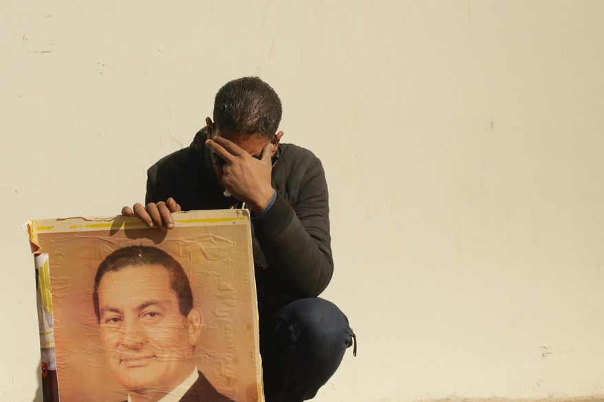A supporter holds a photo of Egypt's ousted autocratic President Hosni Mubarak as he weeps outside the gate of the mosque ahead of his funeral in New Cairo, Egypt, Wednesday, Feb. 26, 2020. Egypt is holding a full-honors military funeral for Mubarak who was ousted from power in the 2011 Arab Spring uprising. Mubarak, 91, died on Tuesday at a Cairo military hospital from heart and kidney complications. (AP Photo/Maya Alleruzzo)