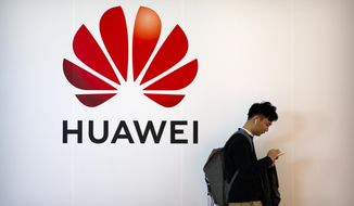 In this Thursday, Oct. 31, 2019, file photo, a man uses his smartphone as he stands near a billboard for Chinese technology firm Huawei at the PT Expo in Beijing. (AP Photo/Mark Schiefelbein, File) **FILE**