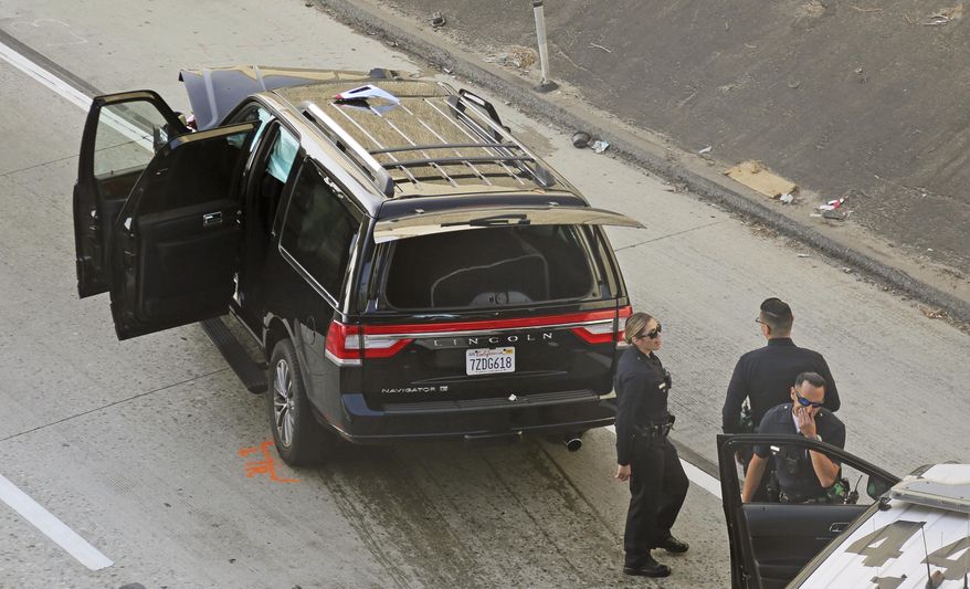 Los Angeles police officers stand after a pursuit of a stolen hearse with with a casket and body inside on Interstate 110 in South Los Angeles Thursday, Feb. 27, 2020. The hearse was stolen from outside a Greek Orthodox church in East Pasadena on Wednesday night. The Los Angeles County Sheriff's Department says one person is in custody. (AP Photo/Reed Saxon)