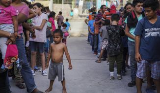 In this Aug. 30, 2019, file photo, migrants, many who were returned to Mexico under the Trump administration&#39;s &quot;Remain in Mexico&quot; program, wait in line to get a meal in an encampment near the Gateway International Bridge in Matamoros, Mexico. (AP Photo/Veronica G. Cardenas, File)
