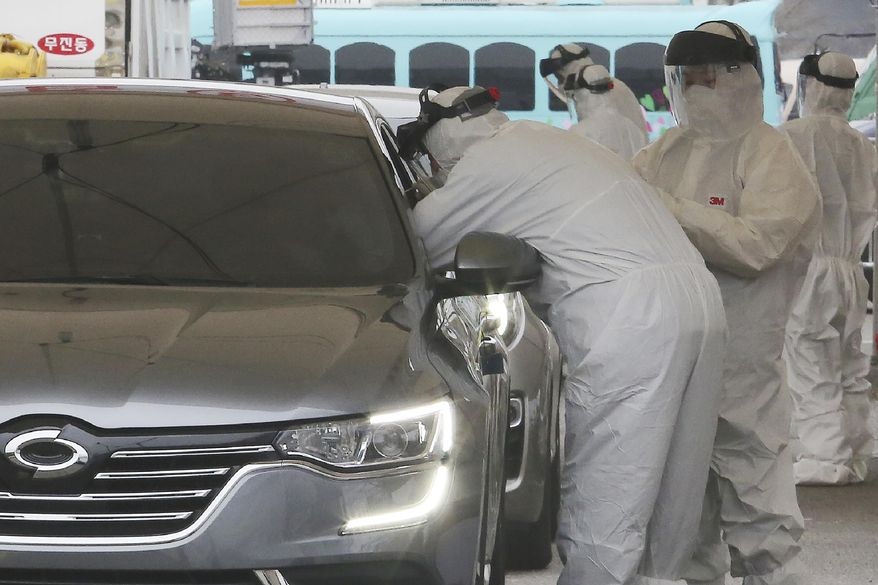 Medical staff wearing protective suits take samples from a driver with symptoms of the coronavirus at a "drive-through" virus test facility in Goyang, South Korea, Sunday, March 1, 2020. The coronavirus has claimed its first victim in the United States as the number of cases shot up in Iran, Italy and South Korea and the spreading outbreak shook the global economy. (AP Photo/Ahn Young-joon)