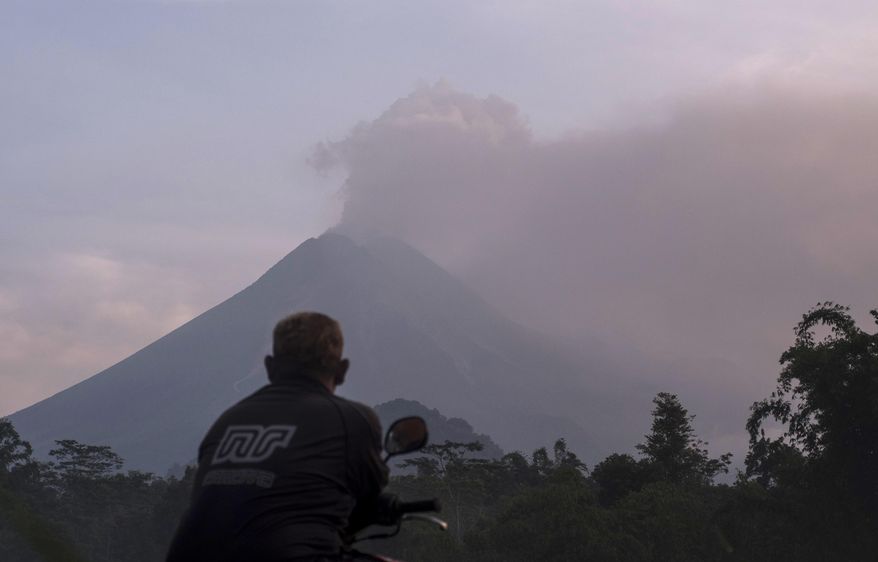 A man watches as Mount Merapi spews volcanic material into the air in Sleman, Indonesia, Tuesday, March 3, 2020. Indonesia's most active volcano erupted Tuesday, spewing sand and pyroclastic material and sending massive smoke-and-ash column into the sky. (AP Photo/Slamet Riyadi)