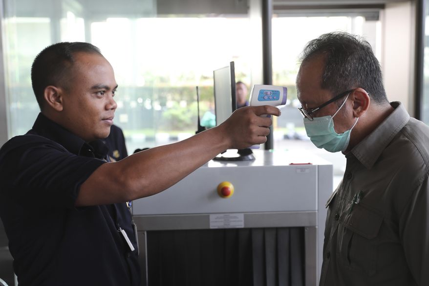 A security official checks the body temperature of a man at a building in Jakarta, Indonesia, Tuesday, March 3, 2020. Indonesia confirmed its first cases Monday, in two people who contracted the illness from a foreign traveler. (AP Photo/Achmad Ibrahim)