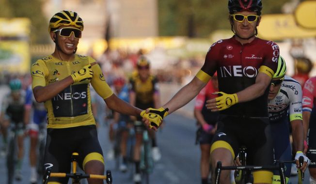 FILE - In this Sunday, July 28, 2019 file photo, Colombia&#x27;s Egan Bernal wearing the overall leader&#x27;s yellow jersey, left, holds hands with Britain&#x27;s Geraint Thomas after winning the Tour de France cycling race in Paris. The team of reigning Tour de France champion Egan Bernal has withdrawn from all races over the next three weeks amid the spread of the new virus outbreak and following the death of one of its sports directors. (AP Photo/Michel Euler, File)