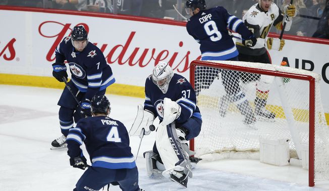 Winnipeg Jets goaltender Connor Hellebuyck (37) makes a save as Dmitry Kulikov (7) and Neal Pionk (4) defend against the Vegas Golden Knights during the first period of an NHL hockey game Friday, March 6, 2020, in Winnipeg, Manitoba. (John Woods/The Canadian Press via AP)