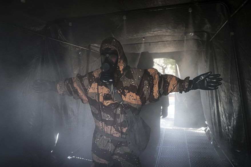 In this Sunday, March 1, 2020, photo, an Iranian army member disinfects his protective gear against the new coronavirus in Tehran, Iran. Wearing gas masks and waterproof fatigues, members of Iran's Revolutionary Guard now spray down streets and hospitals with disinfectants as the Islamic Republic faces one of the world's worst outbreaks of the new coronavirus. (Mahmood Hosseini/Tasnim News Agency via AP)