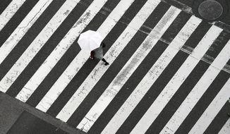 In this Dec. 19, 2019, photo, a woman walks on the pedestrian crossing in the rain in Tokyo. Japan&#39;s economy contracted at a dismal 7.1% annual rate during the October-December period, worse than the initial estimate, raising fears the world&#39;s third largest economy could be headed to a recession. (AP Photo/Eugene Hoshiko)