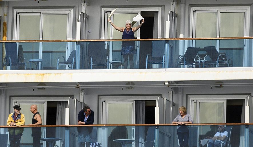 A passenger waves aboard the Grand Princess off the coast of San Francisco as a media boat approaches on Sunday, March 8, 2020. The cruise ship is expected to dock Monday for novel coronavirus quarantine after multiple people tested positive for the virus. (AP Photo/Noah Berger)