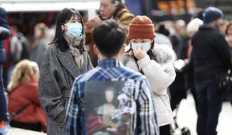 People wearing face masks stand in Piccadilly Circus, London,  Saturday, March 7, 2020. A man in his early 80s has become the second person to die in the UK after testing positive for the coronavirus. (Yui Mok/PA via AP)