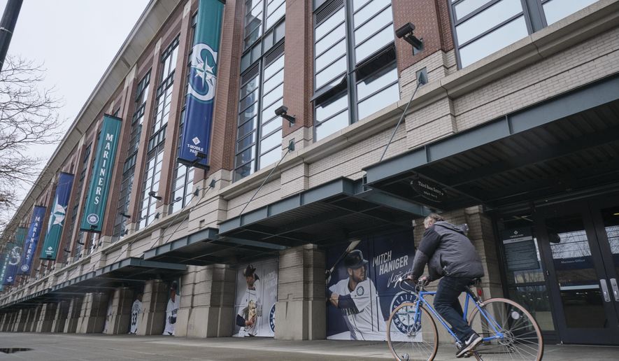 A bicyclist rides past T-Mobile Park, Wednesday, March 11, 2020, in Seattle, where baseball's Seattle Mariners plays home games. In efforts to slow the spread of the COVID-19 coronavirus, Washington State Gov. Jay Inslee announced a ban on large public gatherings in three counties in the metro Seattle area. That decision impacts the Seattle Mariners, Seattle Sounders, and the XFL's Seattle Dragons home games. (AP Photo/Stephen Brashear)