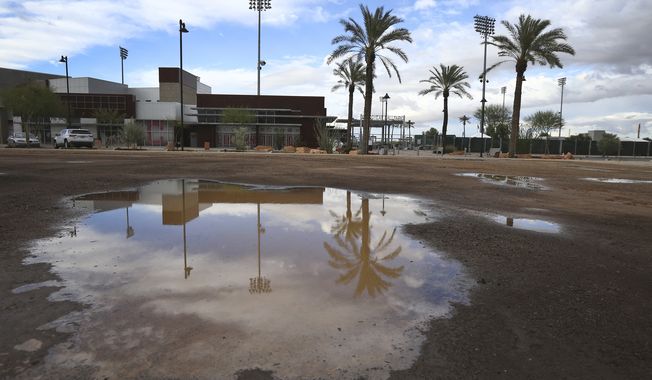 A puddle in an empty parking lot reflects a closed Goodyear Ballpark, home of the Cleveland Indians and Cincinnati Reds baseball teams, Thursday, March 12, 2020, in Goodyear, Ariz. Major League Baseball has suspended the rest of its spring training game schedule because if the coronavirus outbreak. MLB is also delaying the start of its regular season by at least two weeks. (AP Photo/Ross D. Franklin)