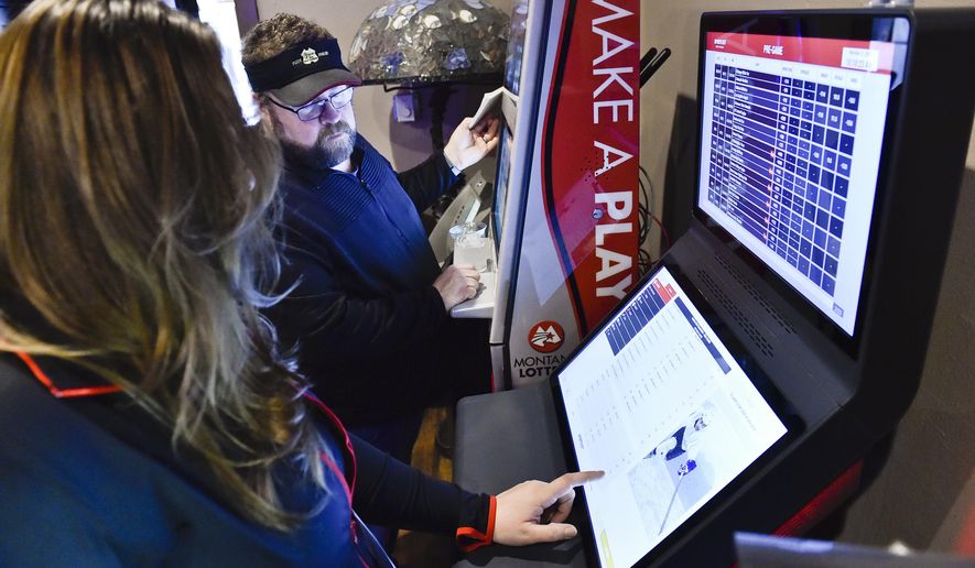 A Montana Lottery employee shows The Rialto Bar Owner, Dax Cetraro, how to operate the Sports Bet Montana kiosk that was installed in the bar Wednesday, March 11, 2020, in Helena, Mont. (Thom Bridge/Independent Record via AP)