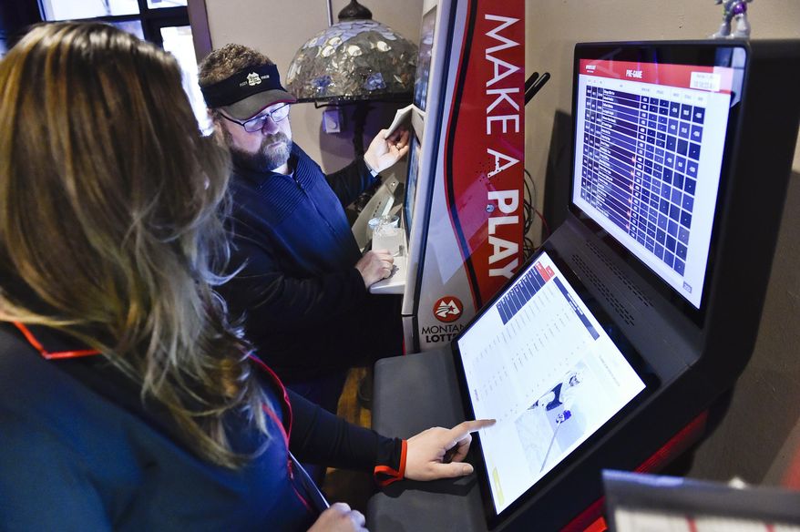 A Montana Lottery employee shows The Rialto Bar Owner, Dax Cetraro, how to operate the Sports Bet Montana kiosk that was installed in the bar Wednesday, March 11, 2020, in Helena, Mont. (Thom Bridge/Independent Record via AP)
