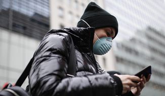 A pedestrian uses her phone while wearing a face mask in New York City&#39;s Herald Square on Thursday, March 12, 2020. (AP Photo/John Minchillo) **FILE**