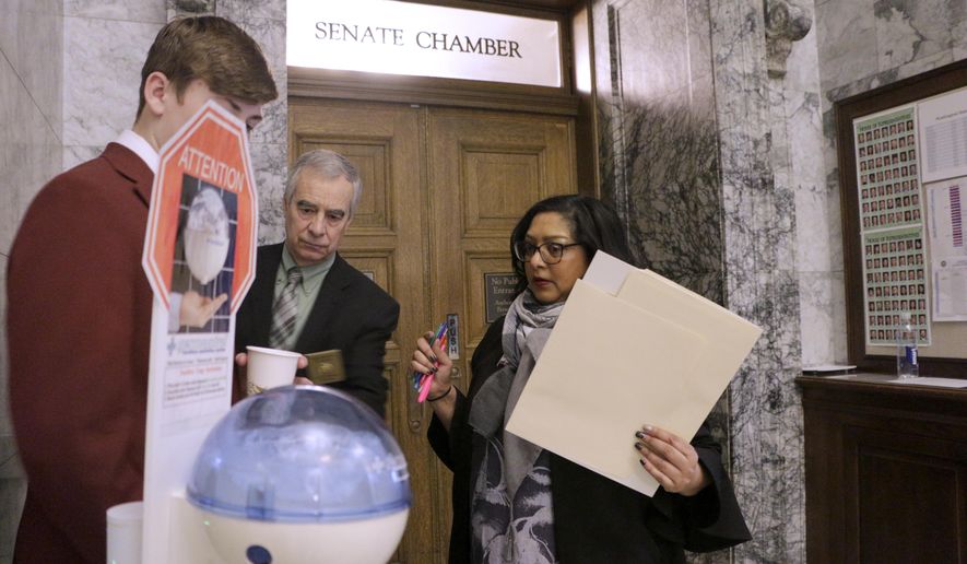 Democratic Sen. Mona Das, far right, talks to a page outside of the Senate chambers, where a hand sanitizing station is set up, Thursday, March 12, 2020, in Olympia. Lawmakers were finishing up their work amid concerns of the state's COVID-19 outbreak. For most people, the new coronavirus causes only mild or moderate symptoms. For some it can cause more severe illness. (AP Photo/Rachel La Corte)