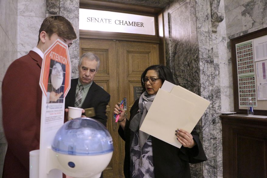 Democratic Sen. Mona Das, far right, talks to a page outside of the Senate chambers, where a hand sanitizing station is set up, Thursday, March 12, 2020, in Olympia. Lawmakers were finishing up their work amid concerns of the state's COVID-19 outbreak. For most people, the new coronavirus causes only mild or moderate symptoms. For some it can cause more severe illness. (AP Photo/Rachel La Corte)