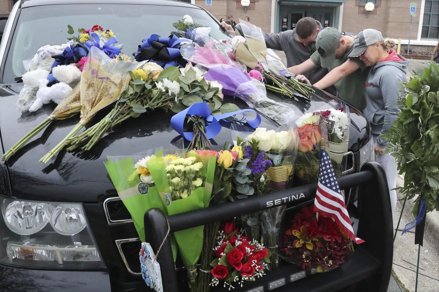 From left, Hot Springs police Officer Shawn Woodall, Officer Cody Rollins and Officer 1st Class Shannon Steed bow their heads in a moment of prayer beside the police unit of Officer 1st Class Brent Scrimshire, who was shot and killed during a traffic stop. (Richard Rasmussen/The Sentinel-Record via AP)