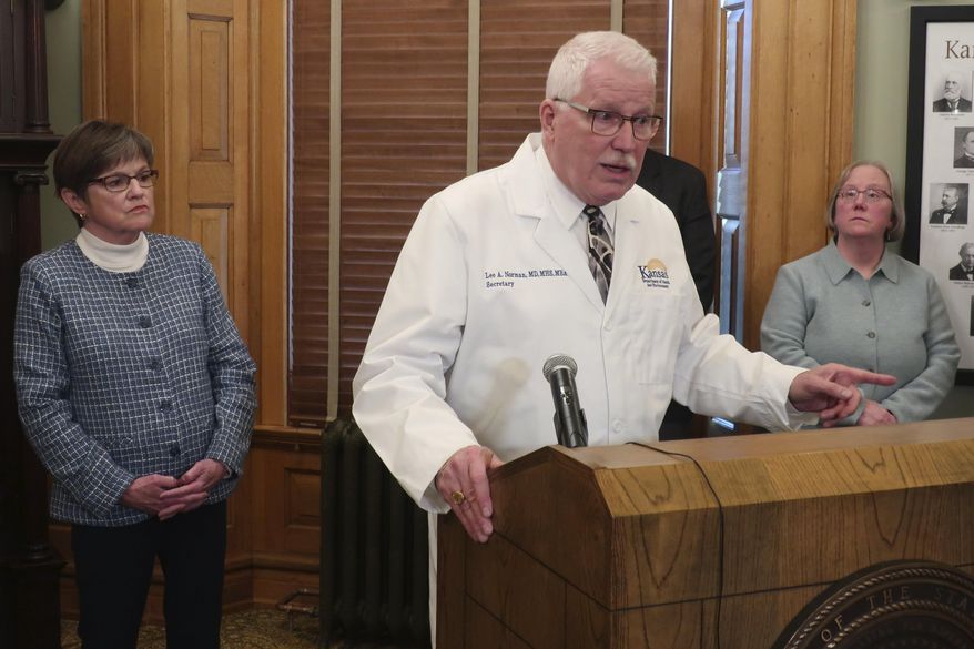 Kansas Health and Environment Secretary Lee Norman, center, answers questions about a COVID-19-related death of a man in his 70s in a Kansas City, Kan., area nursing home, the state's first fatality linked to the coronavirus, Thursday, March 12, 2020, at the Statehouse in Topeka, Kan. Watching are Gov. Laura Kelly, left, and Laura Howard, right, the state's secretary for aging and disability services. (AP Photo/John Hanna)