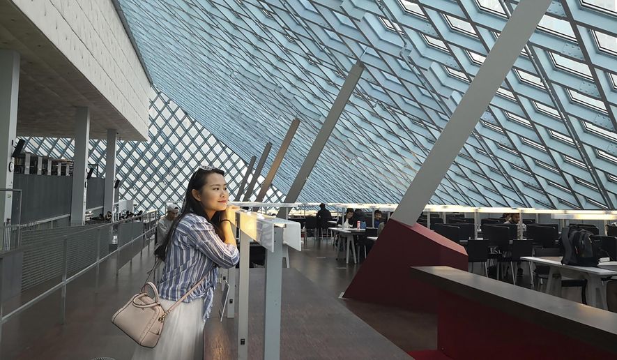 In this August 2019, photo released by Florian Hayek, Courtney Huang, a Chinese citizen living and working in the United States, poses for a photo in the Central Library in Seattle, Wa. Huang is one of hundreds of Chinese whose jobs, lives, and right to work in the U.S. are on the line after the Trump administration imposed a travel ban and visa processing halt on foreigners in China over the coronavirus outbreak. Huang, who aspires to become a U.S. citizen, is worried that she could lose her job and her right to live in the States because her work visa wasn't issued due to the halt. (Florian Hayek via AP)