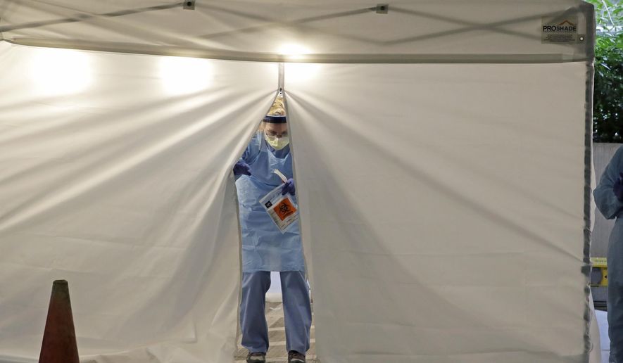 A nurse at a drive up COVID-19 coronavirus testing station set up by the University of Washington Medical Center exits a tent while holding a bag containing a swab used to take a sample from the nose of a person in their car, Friday, March 13, 2020, in Seattle. UW Medicine is conducting drive-thru testing in a hospital parking garage and has screened hundreds of staff members, faculty and trainees for the COVID-19 coronavirus. U.S. hospitals are setting up triage tents, calling doctors out of retirement, guarding their supplies of face masks and making plans to cancel elective surgery as they brace for an expected onslaught of coronavirus patients. (AP Photo/Ted S. Warren)