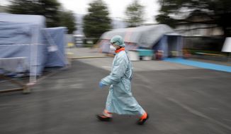 FILE - In this Thursday, March 12, 2020 file photo, a worker wearing a mask and protective clothing walks between the emergency structures that were set up to ease procedures at the Brescia hospital in northern Italy. The medical impact of the new coronavirus is coming into sharper focus in March 2020 as it continues its spread in what is now officially recognized as a pandemic. (AP Photo/Luca Bruno)