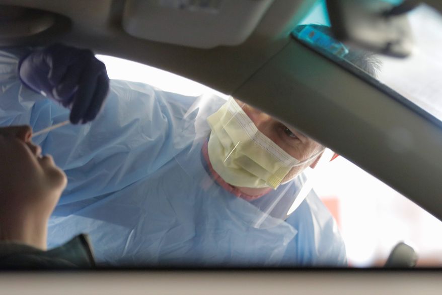A nurse conducts testing for the coronavirus in a hospital parking garage by using a swab to take a sample from the nose of a person in a car.