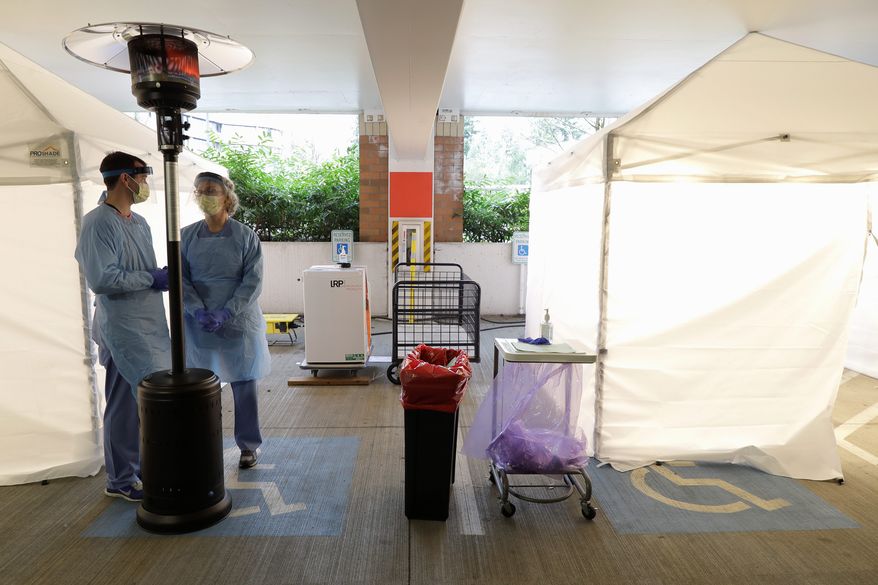 Nurses at a drive-up COVID-19 coronavirus testing station set up by the University of Washington Medical Center wear protective gear as they wait under a heater next to a tent Friday, March 13, 2020, in Seattle. UW Medicine is conducting drive-thru testing in a hospital parking garage and has screened hundreds of staff members, faculty and trainees for COVID-19. U.S. hospitals are setting up triage tents, calling doctors out of retirement, guarding their supplies of face masks and making plans to cancel elective surgery as they brace for an expected onslaught of coronavirus patients. (AP Photo/Ted S. Warren)