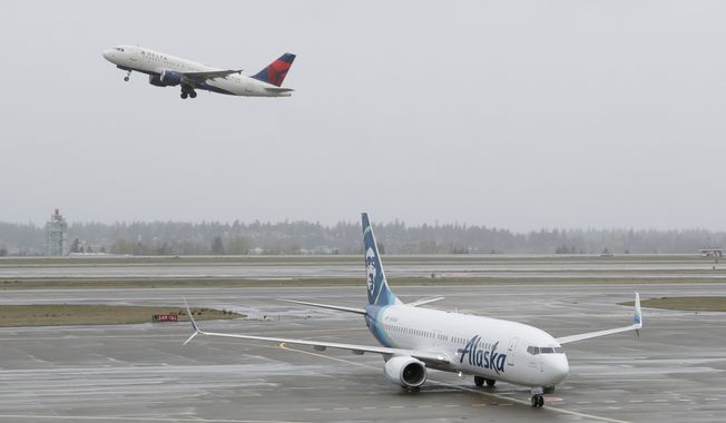 In this April 13, 2018, photo, a Delta Air Lines plane takes off above a taxiing Alaska Airlines airplane at the Seattle-Tacoma International Airport in Seattle.  U.S. airlines are asking the federal government for grants, loans and tax relief that could easily top $50 billion to help them recover from a sharp downturn in travel due to the new coronavirus. Airlines for America, the trade group representing the carriers, posted its request for financial help on Monday, March 16, 2020, just as more airlines around the world were announcing ever-deeper cuts in service and, in some cases, layoffs. (AP Photo/Ted S. Warren) **FILE**