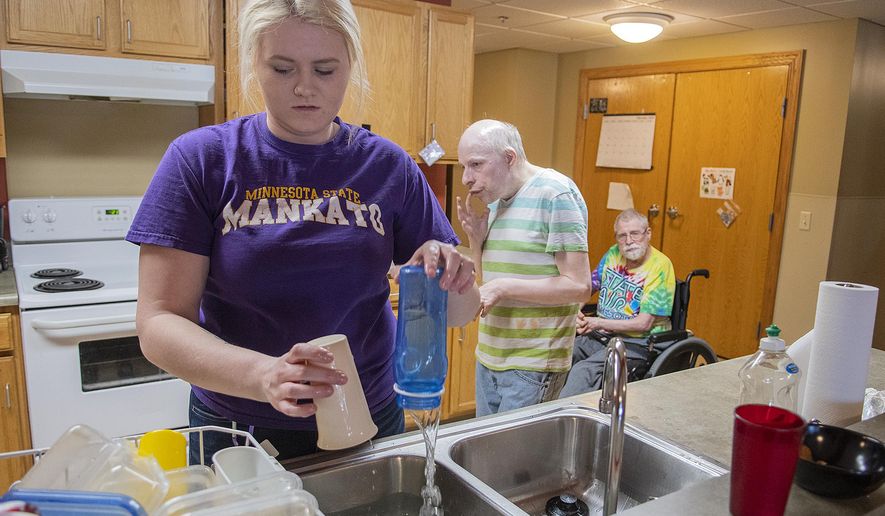 In this Feb. 27, 2020 photo, Wylie Rollings does the dishes in the kitchen in a community room at the Harry Meyering Center in Mankato, Minn., as residents Michael Dreyer and Richard Anderson, right, mull about behind her. (Jackson Forderer/The Free Press via AP)