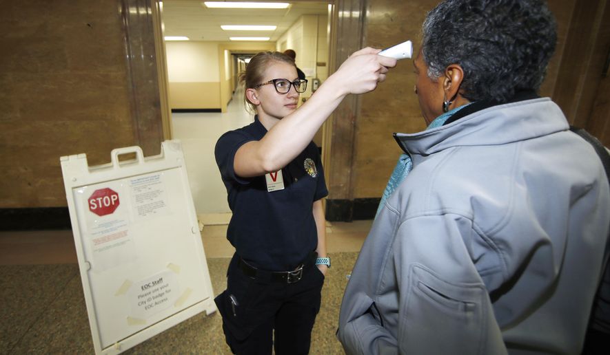 Denver Public Safety Department cadet Savannah Gerace, left, checks the temperature of Denver Deputy Mayor Happy Haynes to fend off the spread of coronavirus as she enters a news conference early Monday, March 16, 2020, in Denver.  (AP Photo/David Zalubowski)