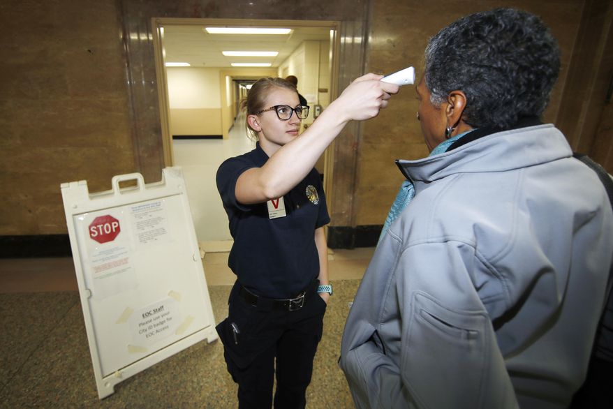 Denver Public Safety Department cadet Savannah Gerace, left, checks the temperature of Denver Deputy Mayor Happy Haynes to fend off the spread of coronavirus as she enters a news conference early Monday, March 16, 2020, in Denver.  (AP Photo/David Zalubowski)