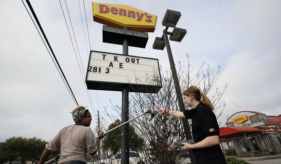 Ieisha Dede, left, and Cali Malatek put up a takeout sign outside a Denny&#39;s restaurant Tuesday, March 17, 2020, in Spring, Texas. Houston area bars and restaurants have been ordered to follow new restrictions for the next 15 days in an effort to curb coronavirus exposure. Bars and nightclubs must close and restaurants can only be open for delivery, pickup and drive-thru services. No in-dining service is allowed. (AP Photo/David J. Phillip) **FILE**