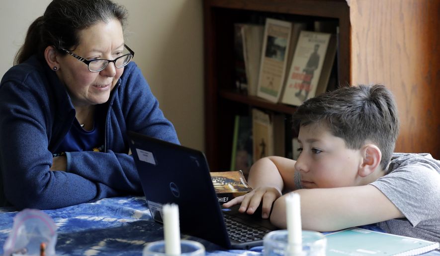 Sarah Marton, para-professional at Niles Township District for Special Education, left, talks with her son Cooper Marton, an 8th grader at Disney II Magnet School, while her son studies school work with his computer at his home in Chicago, Tuesday, March 17, 2020. Illinois Gov. J.B. Pritzker's executive order closes all kindergarten through 12th grade schools — public and private — "for educational purposes" from March 17 through March 30, with students returning to classes March 31 due to caronavirus. Some individual districts, and some other states, have chosen to keep schools closed longer than that. (AP Photo/Nam Y. Huh)