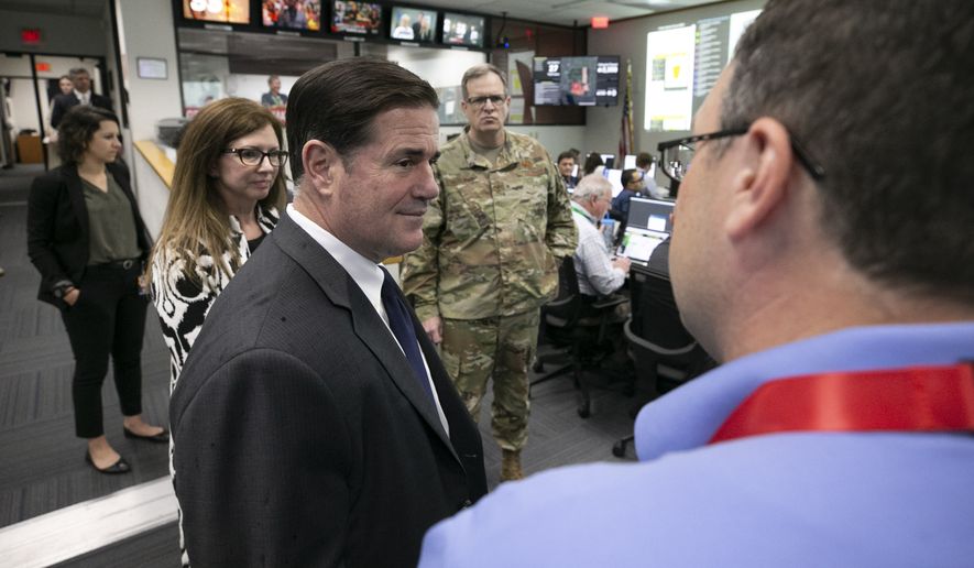 Arizona Gov. Doug Ducey, foreground left, talks to Matt Heckard, right, assistant director of preparedness with the state&#x27;s Department of Emergency and Military Affairs, as members of DEMA work responding to the coronavirus pandemic, in the DEMA operations center at the Arizona National Guard Papago Park Military Reservation in Phoenix on March 18, 2020. Maj. Gen. Michael T. McGuire, background center, the director of DEMA, and Deputy Director Wendy Smith-Reeve, next to Ducey, listen. (David Wallace/The Arizona Republic via AP, Pool)