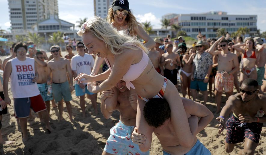 Cece Guida, 19, top, of New York City, pushes on Sam Reddick, 20, of Evansville, Ind., as spring break revelers look on during a game of chicken fight on the beach, Tuesday, March 17, 2020, in Pompano Beach, Fla. As a response to the coronavirus pandemic, Florida Gov. Ron DeSantis ordered all bars be shut down for 30 days beginning at 5 p.m. and many Florida beaches are turning away spring break crowds urging them to engage in social distancing. (AP Photo/Julio Cortez)