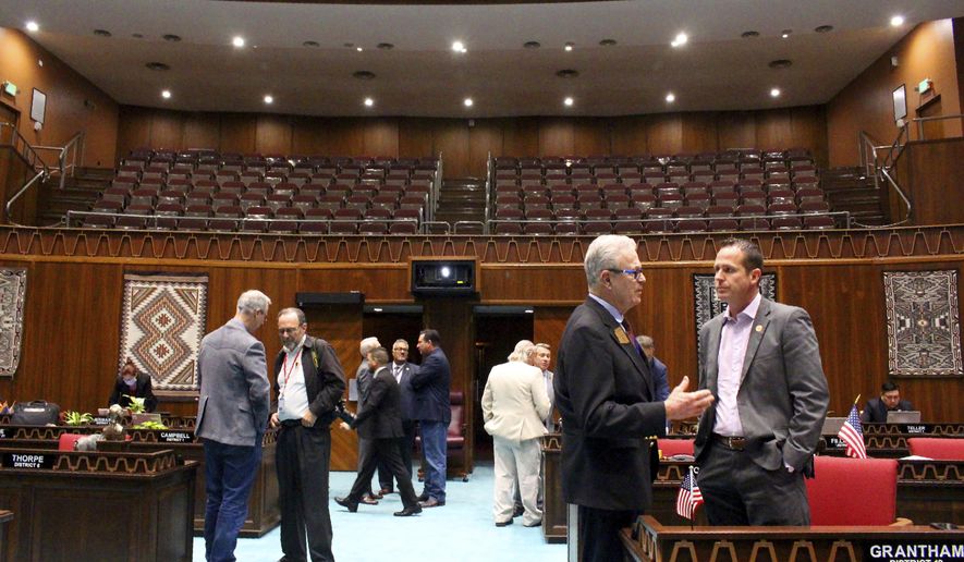 Republican Rep. Noel Campbell, foreground left, speaks with GOP Rep. Travis Grantham, foreground right, as members gather in the Arizona House under a closed public gallery before a floor session at the Capitol in Phoenix, Wednesday, March 18, 2020. The House hopes to quickly pass a bare-bones budget and send it to the Senate before adjourning until the coronavirus crisis ebbs. (AP Photo/Bob Christie)