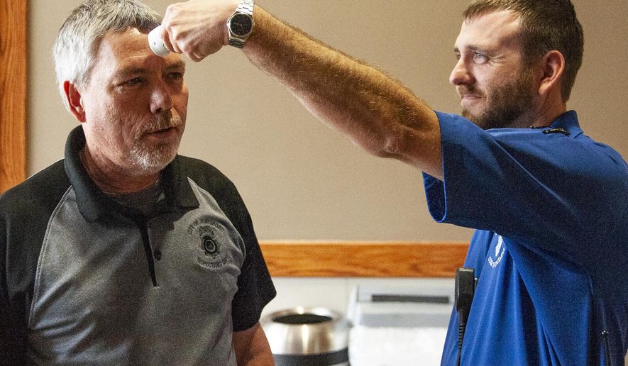 Eric Schmett, right, of the city of Jonesboro Code Enforcement Unit, uses a no-touch forehead thermometer to check the temperature of Troy Doyle as he enters the Municipal Center on Tuesday, March 17, 2020, in Jonesboro, Ark. All city employees and visitors are screened before entering the building as part of a strategy to impede the spread of the coronavirus. (Quentin Winstine/The Jonesboro Sun via AP)