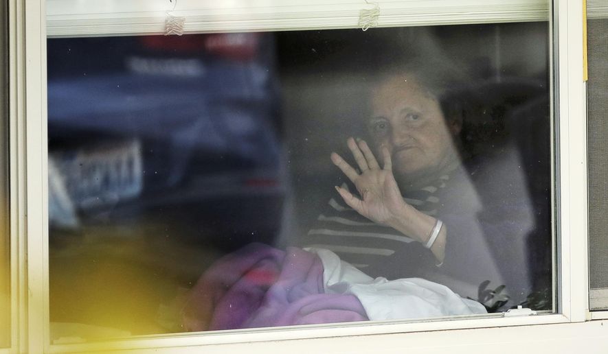 Susan Hailey, who has tested positive for the new coronavirus, waves through the window of her room at the Life Care Center in Kirkland, Wash., as her daughter leaves after a visit, Tuesday, March 17, 2020, near Seattle. In-person visits are not allowed at the nursing home, which has been at the center of the outbreak of new coronavirus in the state. (AP Photo/Ted S. Warren)