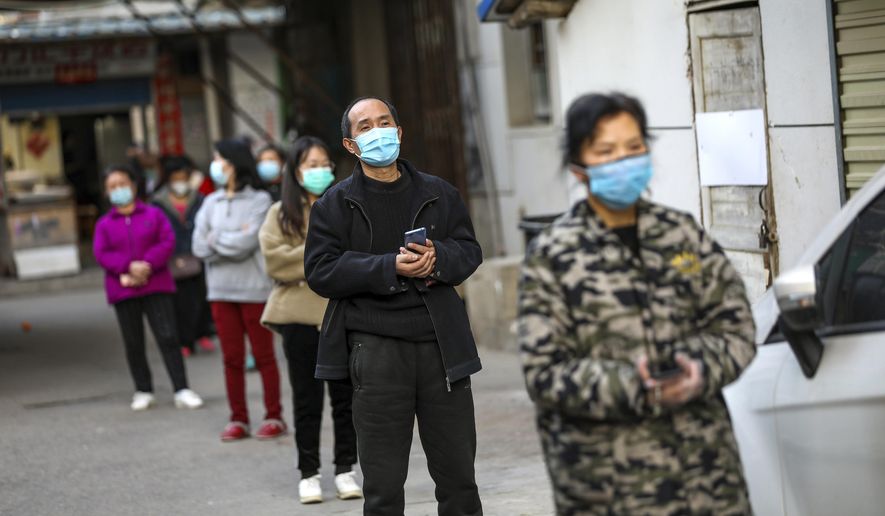 In this March 18, 2020 photo, people stand in a spaced line as they wait to buy pork at the entrance gate of a closed residential community in Wuhan in central China's Hubei Province. Last month, Wuhan was overwhelmed with thousands of new cases of coronavirus each day. But in a dramatic development that underscores just how much the outbreak has pivoted toward Europe and the United States, Chinese authorities said Thursday that the city and its surrounding province had no new cases to report. The virus causes only mild or moderate symptoms, such as fever and cough, for most people, but severe illness is more likely in the elderly and people with existing health problems. (Chinatopix via AP)