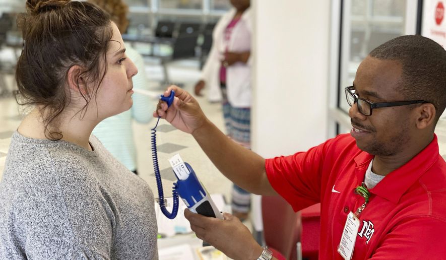 Emma Moffett-Taylor, left, has her temperature taken by OCH Regional Medical Center employee Demarion Jackson at a screening station in the hospital's emergency room, in Starkville, Miss., Wednesday, March 18, 2020. All visitors to the hospital are screened, which includes checking temperature and answering a questionnaire concerning recent travel and contact with those possible exposed to COVID-19, more commonly referred to as the coronavirus. (Ryan Phillips/The Starkville Daily News, via AP)
