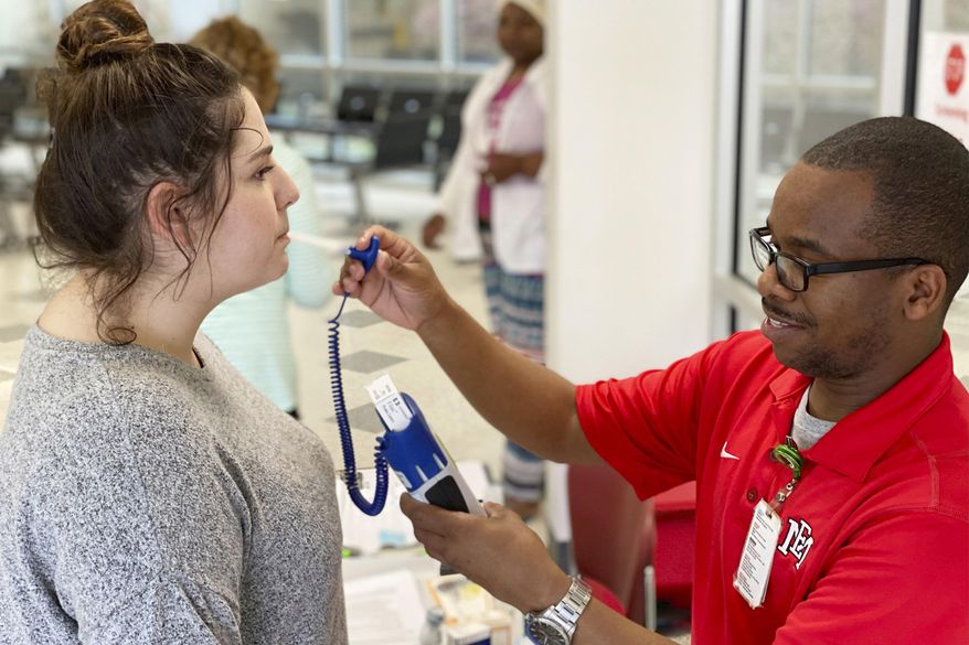 Emma Moffett-Taylor, left, has her temperature taken by OCH Regional Medical Center employee Demarion Jackson at a screening station in the hospital's emergency room, in Starkville, Miss., Wednesday, March 18, 2020. All visitors to the hospital are screened, which includes checking temperature and answering a questionnaire concerning recent travel and contact with those possible exposed to COVID-19, more commonly referred to as the coronavirus. (Ryan Phillips/The Starkville Daily News, via AP)