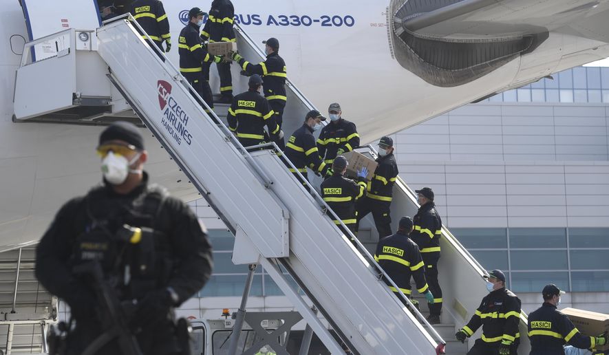 A police officer holds a gun as firefighters unload an airplane after its arrival at the Vaclav Havel Airport in Prague, Friday, March 20, 2020. The airplane brought medical aid and protective materials against coronavirus from China. (Michal Kamaryt/CTK via AP)