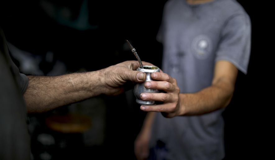 In this March 17, 2020 photo, Oscar Brun, left, shares his "mate" drink with a work colleague Tomas Bravo at his ironworks shop in Buenos Aires, Argentina. Brun said one prepares "mate" to share it and be social. Brun, who has lived in Argentina for decades, works with two other men in a small blacksmith shop in Buenos Aires. He continues to share his "bombilla" with one of his colleagues - the small metal tube through which the mate is sipped. The other, on the other hand, is reluctant to do so since the outbreak of the new coronavirus or COVID-19. (AP Photo/Natacha Pisarenko)