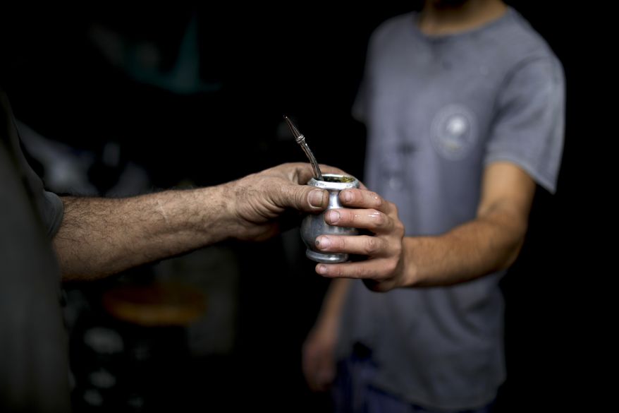 In this March 17, 2020 photo, Oscar Brun, left, shares his "mate" drink with a work colleague Tomas Bravo at his ironworks shop in Buenos Aires, Argentina. Brun said one prepares "mate" to share it and be social. Brun, who has lived in Argentina for decades, works with two other men in a small blacksmith shop in Buenos Aires. He continues to share his "bombilla" with one of his colleagues - the small metal tube through which the mate is sipped. The other, on the other hand, is reluctant to do so since the outbreak of the new coronavirus or COVID-19. (AP Photo/Natacha Pisarenko)