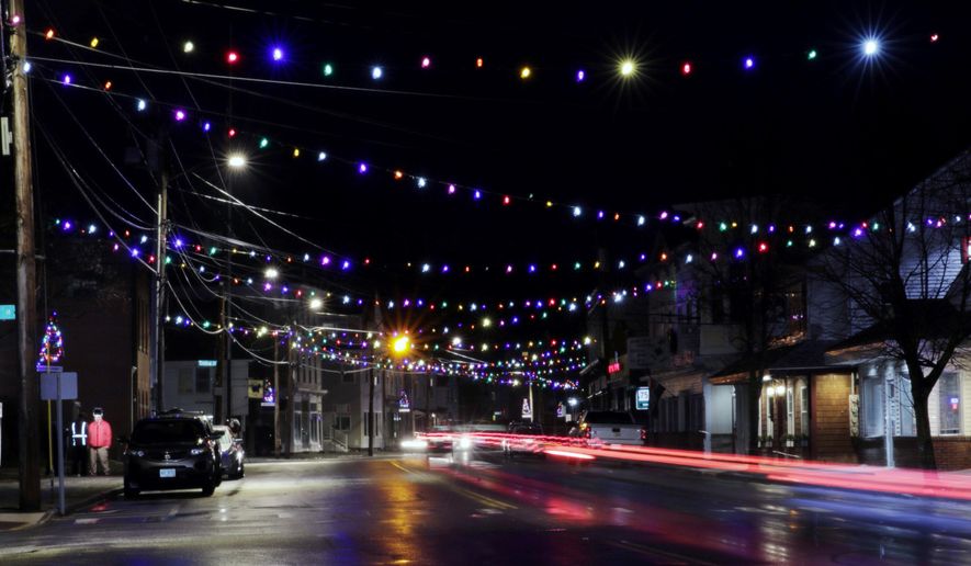 In this March 19, 2020, photo, car tail lights streak under Christmas lights recently turned back on in Farmington, N.H. As the coronavirus spreads, holiday lights are going back up to provide a bit of emotional and actual brightness. (AP Photo/Charles Krupa)