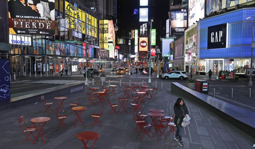 In this March 16, 2020 file photo, a woman walks through a lightly trafficked Times Square in New York, March 16, 2020. As of Sunday, nearly 2,000 people with the virus have been hospitalized in the state of New York and 114 have died, officials said. More than 15,000 have tested positive statewide, including 9,000 in New York City. (AP Photo/Seth Wenig)