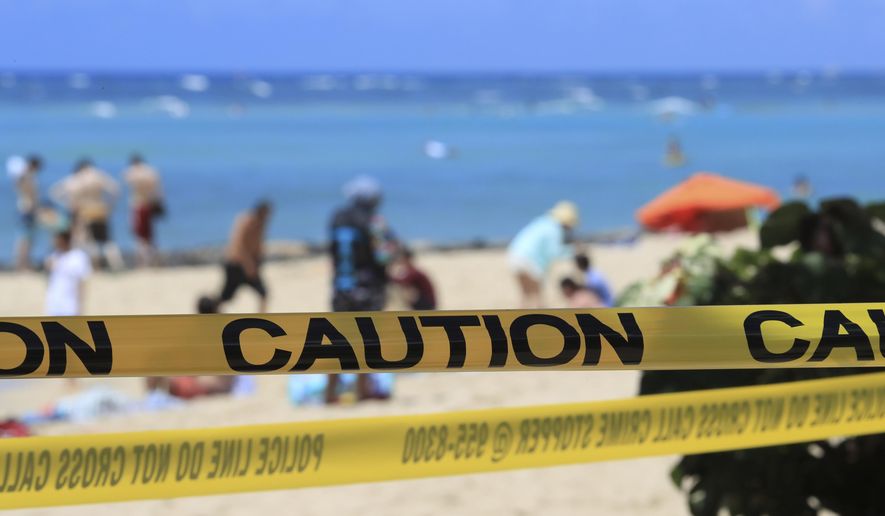 FILE - In this Friday, March 20, 2020, file photo, as beachgoers are seen in the background, yellow caution tape wrapped across Waikiki in Honolulu. Hawaii's governor has instituted a mandatory 14-day self quarantine starting Thursday, March 27, of all people traveling to the state as part of efforts to fight the spread of coronavirus. The order applies to returning residents, as well as visitors. (AP Photo/Marco Garcia, File)
